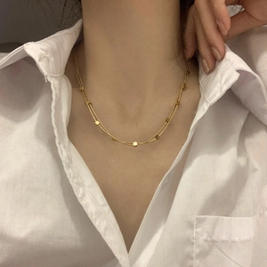 Close-up of a double-layered gold square bead necklace worn on a woman's collarbone