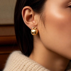 Detailed close-up of matte 18K gold apple earring with sparkling crystal on a model