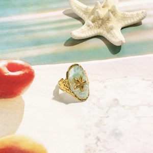 Gold starfish ring with light blue pearlescent inlay on a coastal beach style background