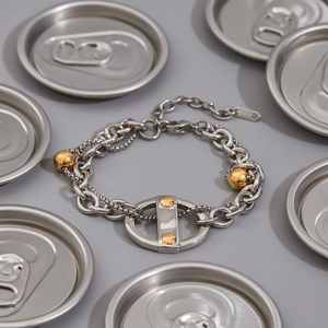 Détail du bracelet en chaîne argentée avec sphères dorées et maillon ovale sur gris