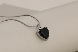 Macro detail of a silver snake chain necklace featuring a heart-shaped black crystal pendant