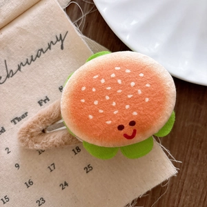 Close-up of a plush burger hair clip with a cute smile face on a beige fabric background