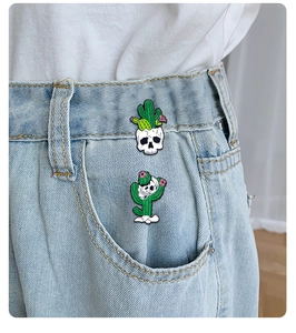 Detail view of punk style skull and cactus enamel pins on light blue denim jeans fabric