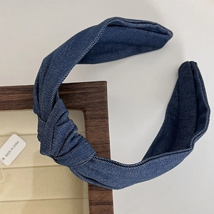 Detail of blue denim wide headband with knotted design on a beige jewelry tray