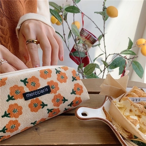 Orange floral corduroy pouch with a black label on a rustic wooden desk