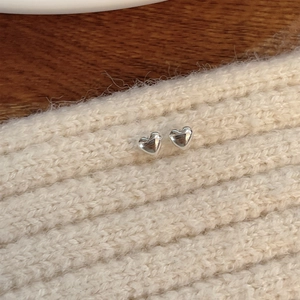 Macro detail of silver heart stud earrings on soft knit fabric and wood background