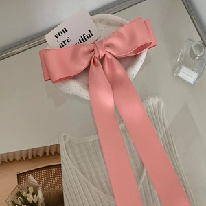 Detail of a large pink satin bow hair clip with long ribbons on a ceramic tray