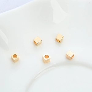 Perles intercalaires cubes en or 14K pour bijoux DIY sur un plateau en céramique blanc