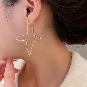 Close-up of a gold cross star earring worn on model for a minimalist fashion look