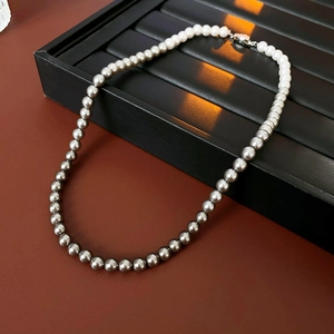 Detailed close-up of white and grey pearl necklace on a premium black jewelry display tray