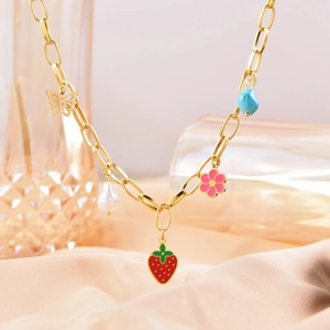 Detail of gold chain necklace with strawberry, butterfly, and flower pendants on silk fabric