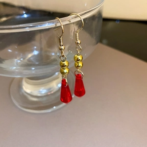 Detail view of red waterdrop earrings with golden hooks hanging on a clear glass rim