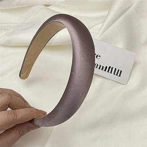 Close-up of a thick dusty purple satin headband with soft sponge padding on a silk background