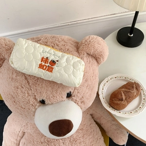 Close-up of quilted cream pouch featuring orange persimmon embroidery on a soft bear background