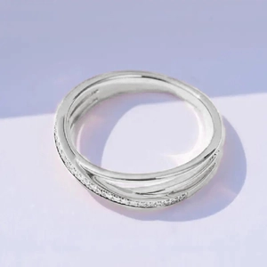 Detailansicht eines silbernen Crossover-Rings mit Mikro-Zirkonia-Besatz auf lila Hintergrund