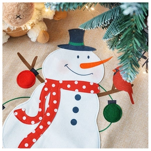 Detail of plush snowman with red polka dot scarf on rustic linen Christmas tree skirt