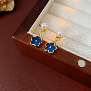 Macro shot of gold floral earrings with blue enamel petals and a pearl drop on velvet