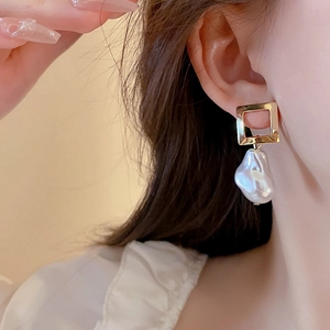 Detail of gold square frame earring with irregular pearl drop worn by a female model