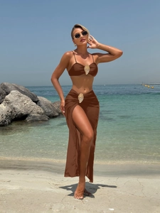 Three-piece brown bikini set with metallic shell buckles and matching beach sarong