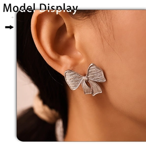 Close-up of silver bow stud earrings with brushed metal texture on female model's ear