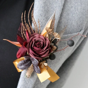 Vintage-Ansteckblume mit burgunderroter Kunstrose und goldenen Akzenten auf grauem Revers