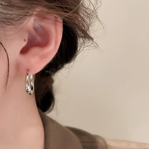 Close-up of polished silver C-shape metal hoop earring worn on model for a minimalist look
