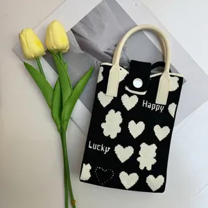 Detail of knitted phone bag with heart pattern and Happy Lucky woven text