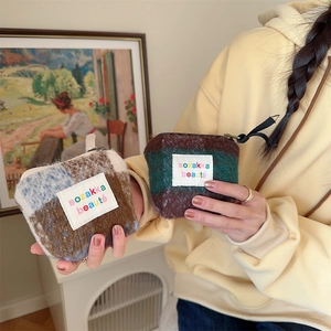Mini plush patchwork cosmetic bag with zipper and logo label held by a hand