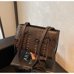 Vintage brown PU leather handbag with silver rivets and woven tassels on an art book