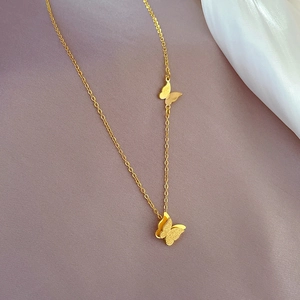 Detail of gold butterfly necklace with dual pendants on soft grey textured fabric