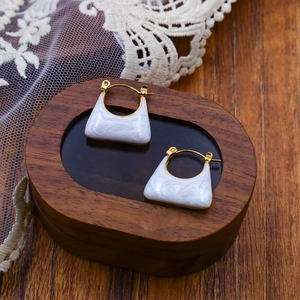 Dettaglio di orecchini a forma di borsa con trama in marmo bianco e finiture oro