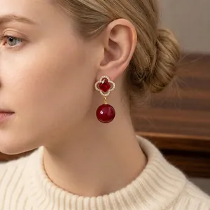 Elegant gold four-petal flower earrings with red stones and pearls worn by a model