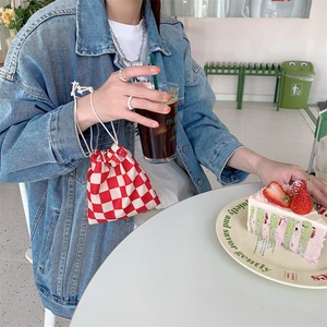 Primer plano de una bolsa con cordón a cuadros rojos y blancos usada como bolso de mano