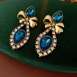 Vintage gold bow earrings with blue teardrop stones and rhinestones on green velvet