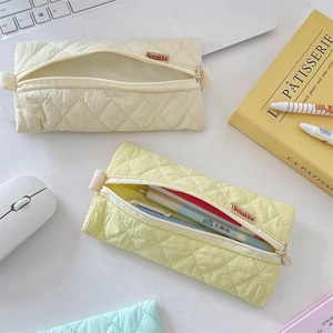 Quilted pastel pencil cases in cream and yellow colors on a desk with a laptop