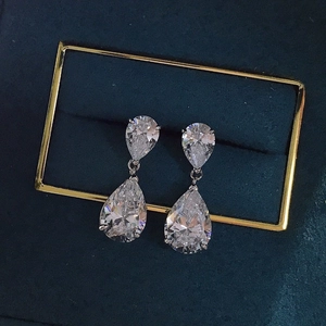 Macro shot of silver teardrop earrings with pear-cut zircon stones on green velvet