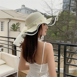 Detail of a beige straw sun hat featuring elegant black and white trim with pearl accents