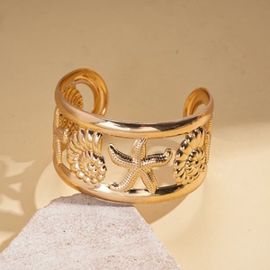 Detail of golden open cuff bracelet with ocean star, shell and hollowed metal texture