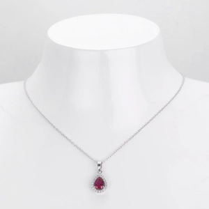 Macro shot of a teardrop-shaped ruby red pendant with white zircon halo on a silver chain