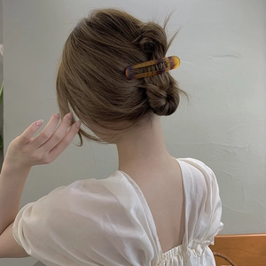 Close-up of a matte tortoiseshell rectangular hair claw clip worn in a low bun hairstyle