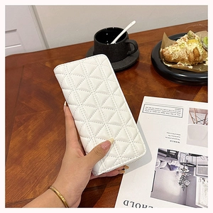 Detail of white quilted long wallet with diamond lattice pattern held in hand