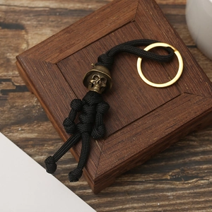 Handmade black paracord keychain with bronze skull bead and gold ring on wooden base