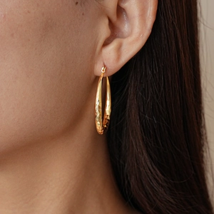 Macro view of gold hoop earring with geometric diamond texture on female model ear