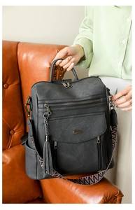 Detail of grey PU leather backpack with tassel charm and woven shoulder strap on sofa