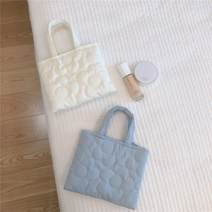 Dettaglio della trama floreale trapuntata su mini borse imbottite in beige e azzurro