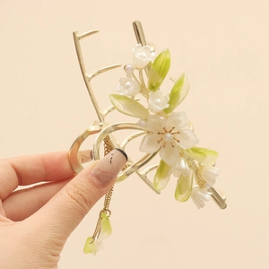 Detail view of golden flower hair claw clip with white blossoms and hanging pearl tassel