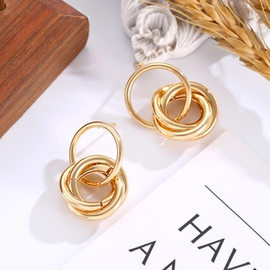 Detailed close-up of intertwined gold circle earrings on a rustic wood and wheat base