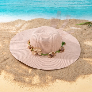 Detail of pink straw sun hat with floral wreath and mesh ribbon on sunny beach