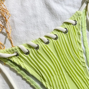 Detail of light green ribbed bikini fabric featuring white lace-up ties and silver grommets