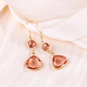 Detailed view of gold earrings with drop-shaped amber crystals on silk fabric